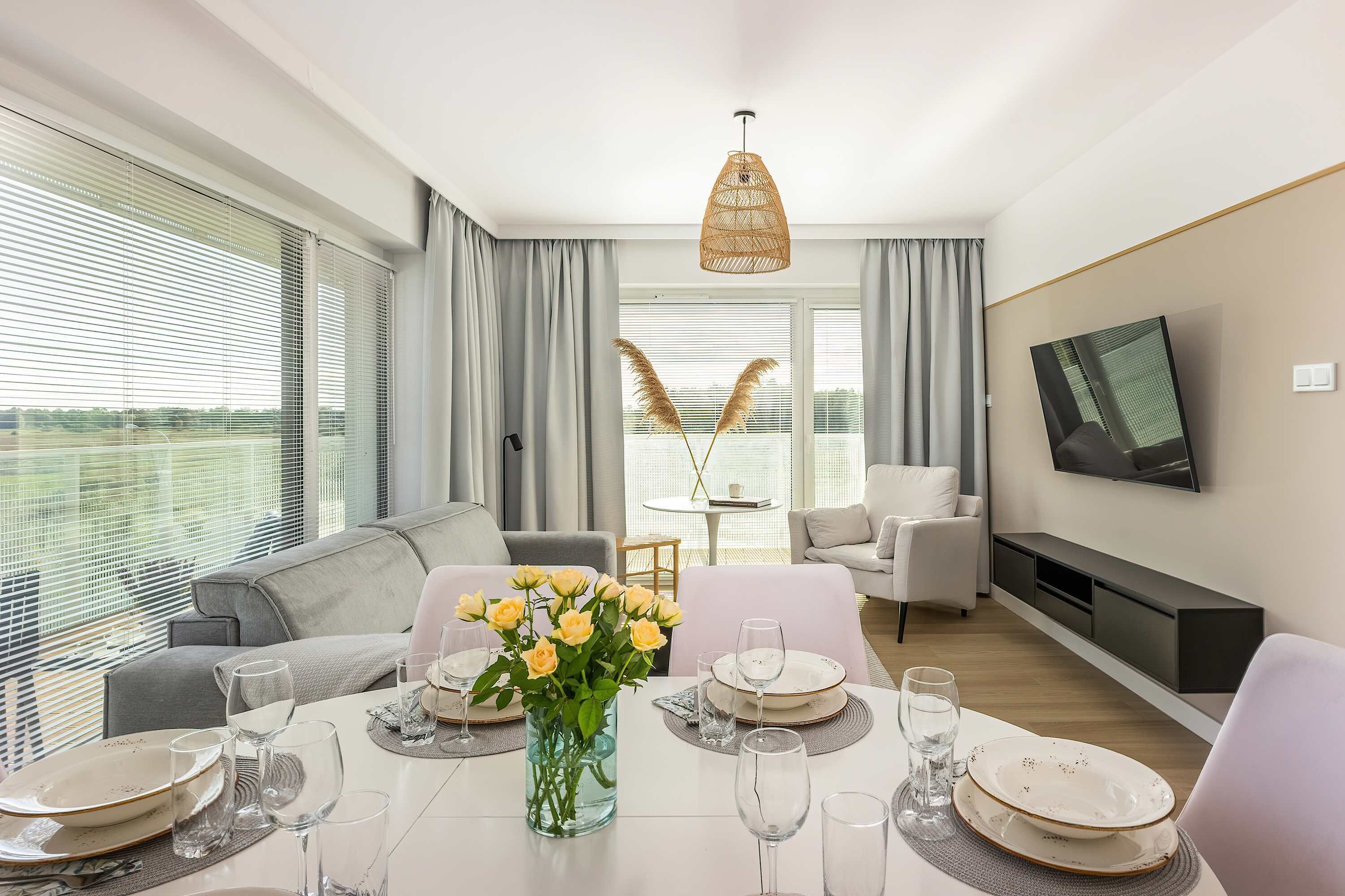 A modern living room with a dining area, large windows, a television, and a fireplace.