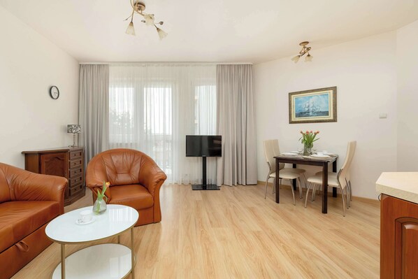 A modern living room with leather sofas, a flat-screen TV, a dining table with chairs, and a painting on the wall.