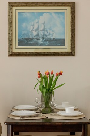 A dining table with white plates, cutlery, and glasses, a vase with tulips, and a framed painting of a sailing ship.