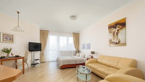 Una habitación de hotel moderna con cama, sofá, mesa de centro de cristal, televisor y obras de arte en las paredes.