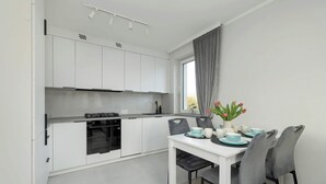 A modern kitchen with white cabinets, a black oven, and a dining area with a white table and grey chairs.