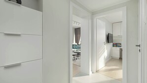 A modern, well-lit hallway with white walls and doors leading to a dining area and a kitchen.