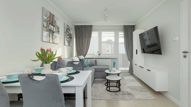 A modern living room with a sofa, dining table, and a TV mounted on the wall.