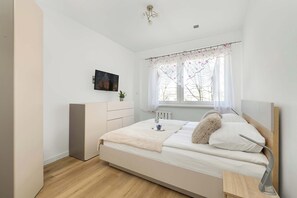 Ein Schlafzimmer mit Bett, Nachttisch, Lampe und einem Fenster mit Vorhängen.