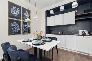 Un comedor con una mesa blanca, sillas azules y un jarrón con flores. En la pared, hay impresiones enmarcadas de motivos botánicos.