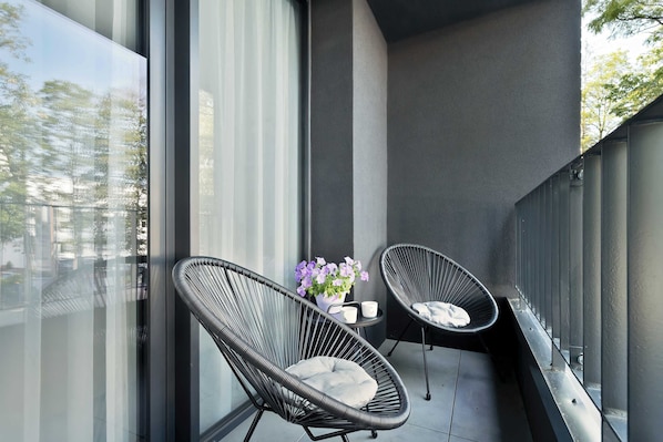 A balcony with two black wire-framed chairs, a small table with a vase of flowers, and a potted plant.