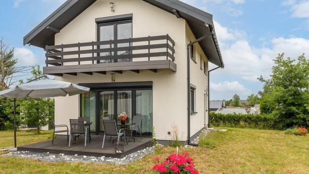 Ein modernes, zweistöckiges Haus mit Balkon, Terrasse und Garten mit roten Blumen.
