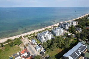 Luftaufnahme einer Küstenlandschaft mit Strand, Gebäuden und einem Steg.