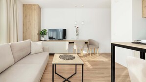 A modern living room with a sofa, a coffee table, a TV, and a dining area with chairs and a table.
