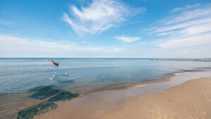 A beach with clear water, a pier extending into the sea, and a sandy shore.