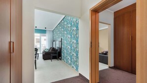 A hallway with a carpeted floor, a wooden door, and a wall with a floral pattern.