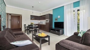 A living room with a sofa, a coffee table with fruit, a TV, and a kitchen in the background.