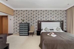 Ein Hotelzimmer mit einem Bett, einem Sessel, einem Schminktisch und einem Fernseher.