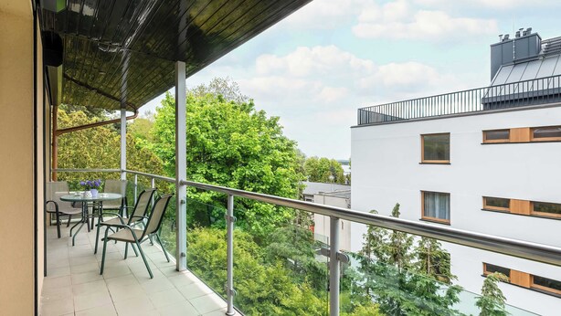 A balcony with a table and chairs, overlooking a cityscape with trees and buildings.