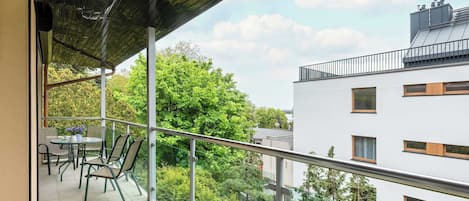 A balcony with a table and chairs, overlooking a cityscape with trees and buildings.