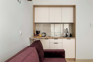 En kompakt opholdsstue med tekøkken, sofa og et vindue.