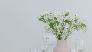 A dining table with white plates, glasses, and a pink vase with flowers.