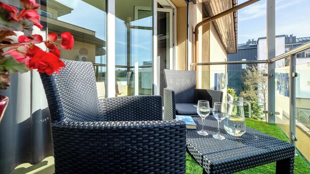 A balcony with wicker furniture, a glass table with drinks, and a view of buildings.