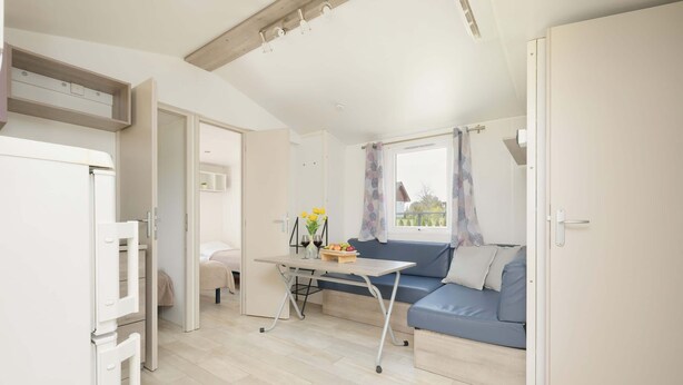 Un espacio habitable compacto con kitchenette, una mesa de comedor, un sofá y un ventanal con cortinas.