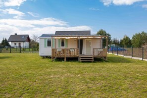 Een stacaravan met een veranda, een omheinde tuin en een aangrenzend huis.