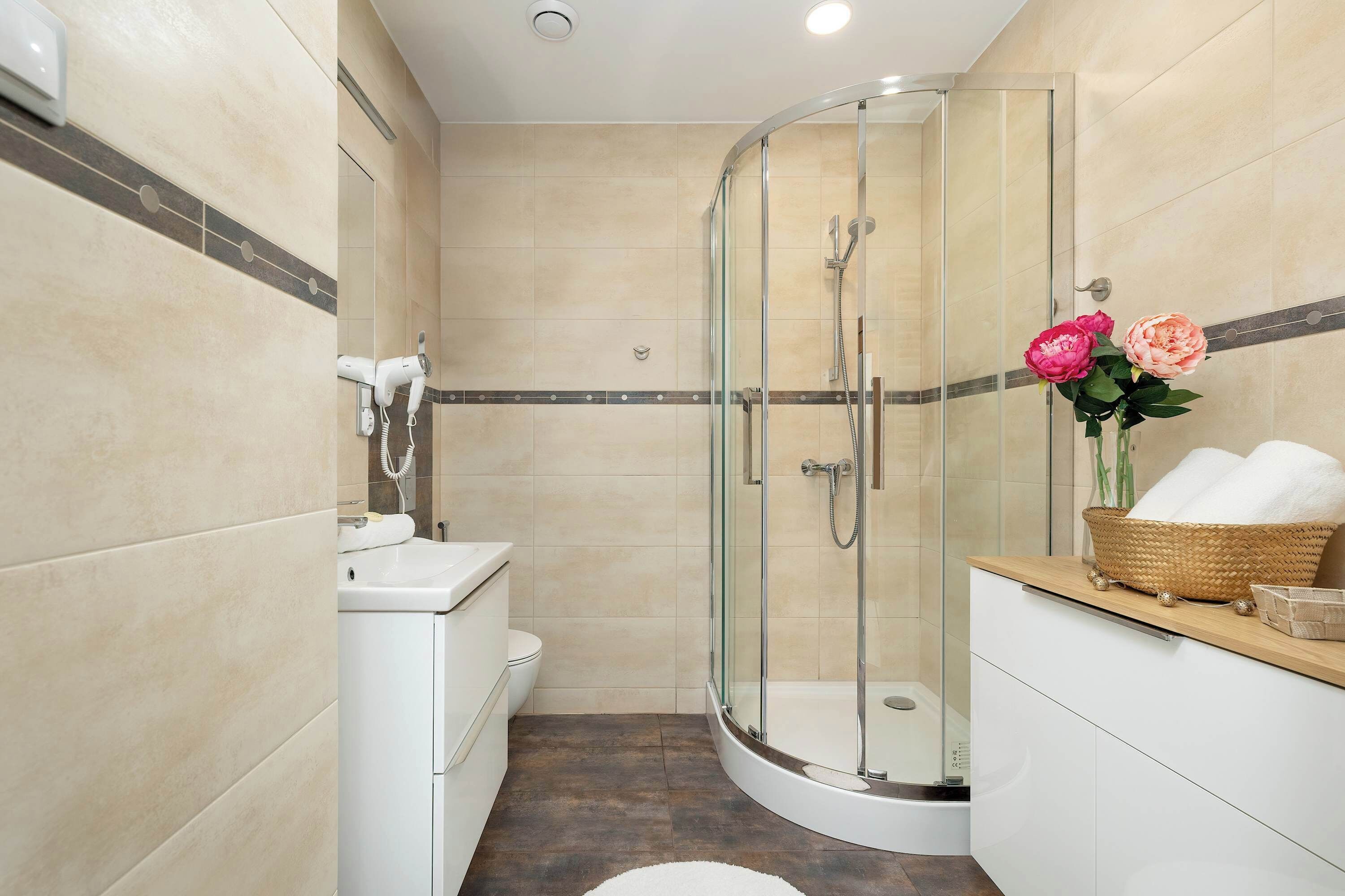 A bathroom with a glass-enclosed shower and modern fixtures. Light tiles give the room a clean and spacious feel. The layout is practical and stylish.
