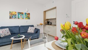 Ein modernes Wohnzimmer mit einem blauen Sofa, zwei Bildern, einem kleinen Tisch mit einer Vase und einem Weinglas.