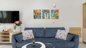 Ein modernes Wohnzimmer mit einem blauen Sofa, zwei passenden Kissen, einem Flachbildfernseher und drei farbenfrohen Bildern an der Wand.