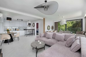 A modern living room with a large sectional sofa, a round coffee table, and a dining area with a table and chairs.