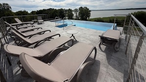 Un área de piscina en la azotea con sillones reclinables, una mesita y vistas a un lago.