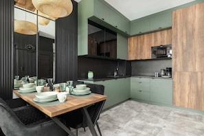 A modern kitchen with green cabinets, a wooden dining table set with plates and glasses, and a black-framed clock on the wall.