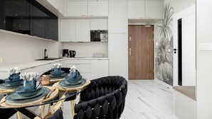 A modern kitchen with white cabinetry, a black upholstered chair, and a dining table set with blue dishes.