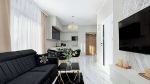 A modern living room with a black sofa, a glass coffee table, and a flat-screen TV mounted on the wall.
