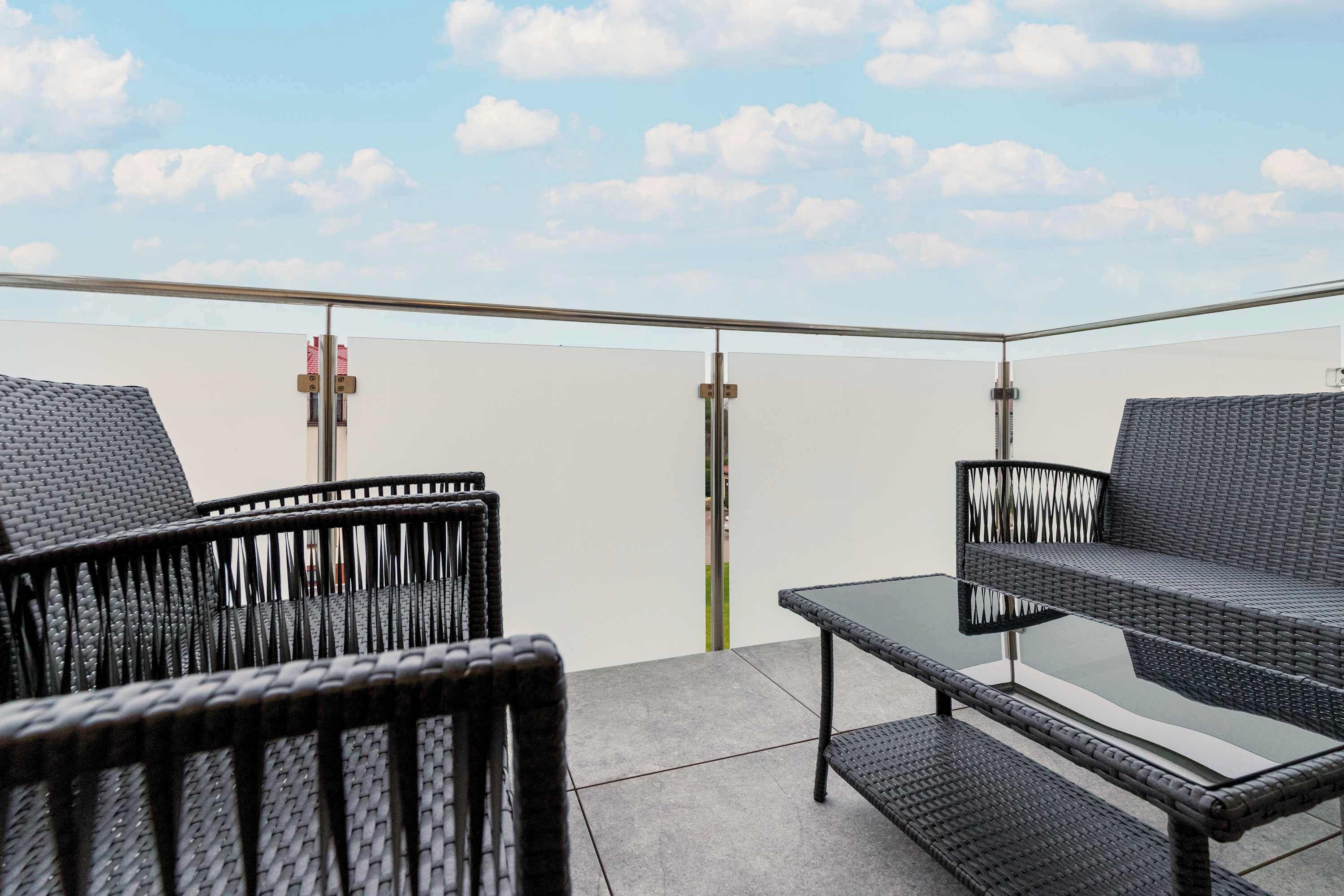 Un balcone con mobili in vimini, un tavolino in vetro e una vista aperta sul cielo.
