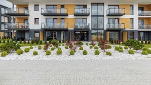 Een modern woongebouw met meerdere verdiepingen, balkons, een aangelegde tuin en een verhard entreegebied.