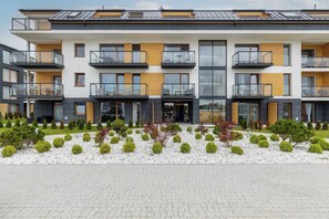 A modern multi-story residential building with balconies, a landscaped garden, and a paved entrance area.