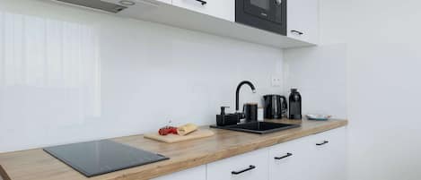 A modern kitchen with white cabinets, a black microwave, a wooden countertop, a black induction cooktop, a sink, and a coffee maker.