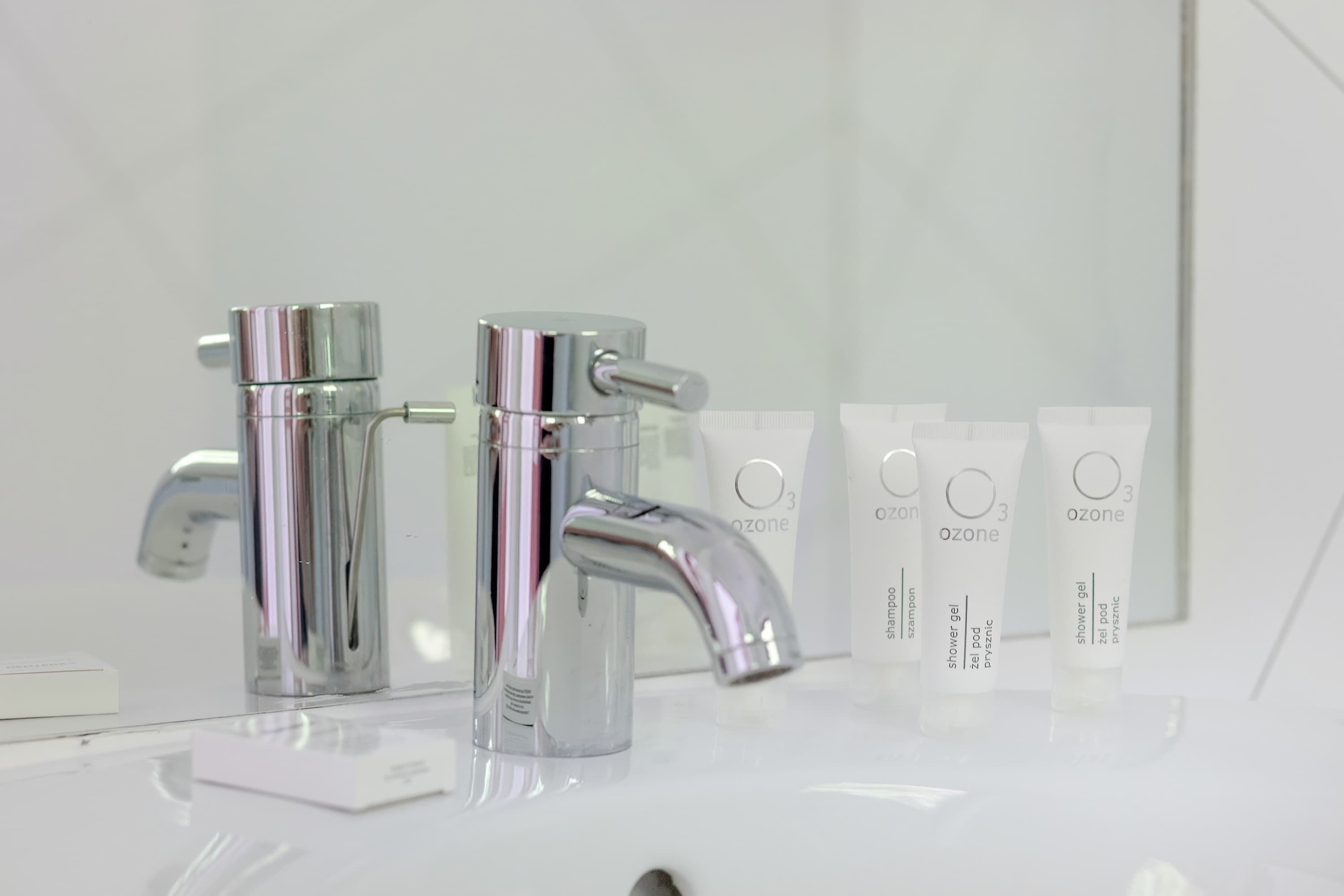 Un baño moderno con grifos cromados, un espejo y varias botellas de gel de ducha Ozone.