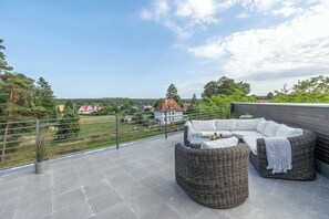 Una terrazza sul tetto con un salotto in vimini, una pianta in vaso e vista sul paesaggio circostante.
