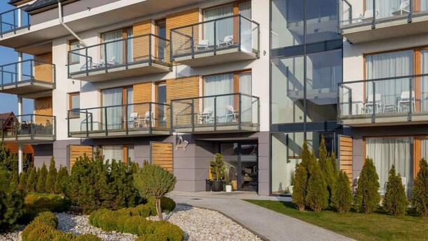 A modern multi-story hotel with balconies, large windows, and a well-maintained garden.