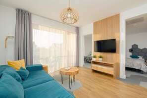 Una sala de estar moderna con un sofá, una mesa de centro redonda de madera, un televisor montado en una pared de madera y una cama con cabecera geométrica.