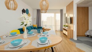 A modern living room with a dining area, wooden furniture, and a large window with curtains.