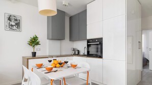 Una cocina moderna con armarios blancos, una mesa de comedor con sillas anaranjadas y una planta en maceta.