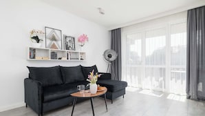 Una sala de estar moderna con un sofá negro, una mesa de centro con un jarrón de flores, una estantería y un ventilador de pie.