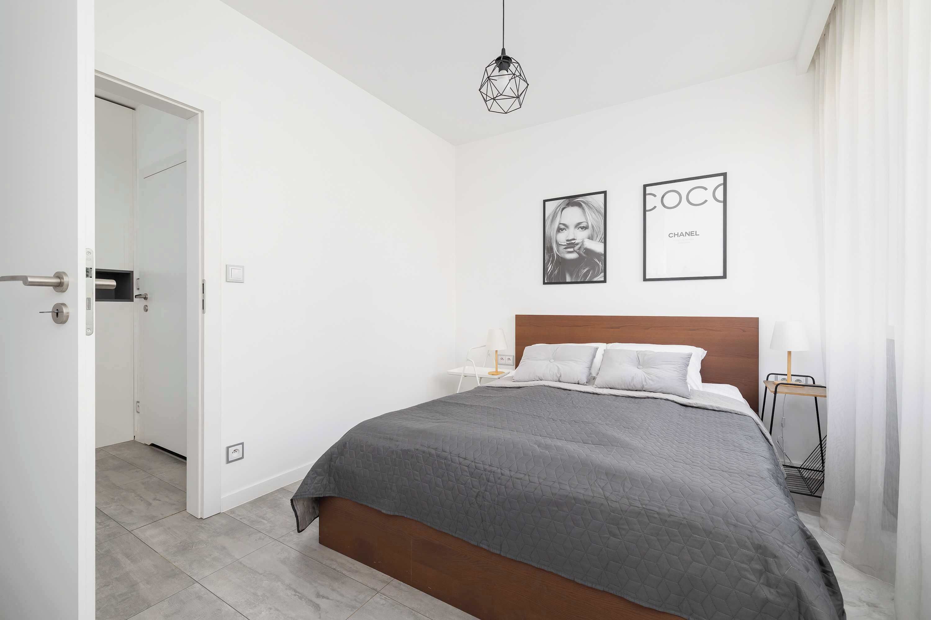 A modern bedroom with a large bed, a geometric pendant light, and two framed pictures on the wall.