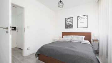 A modern bedroom with a large bed, a geometric pendant light, and two framed pictures on the wall.