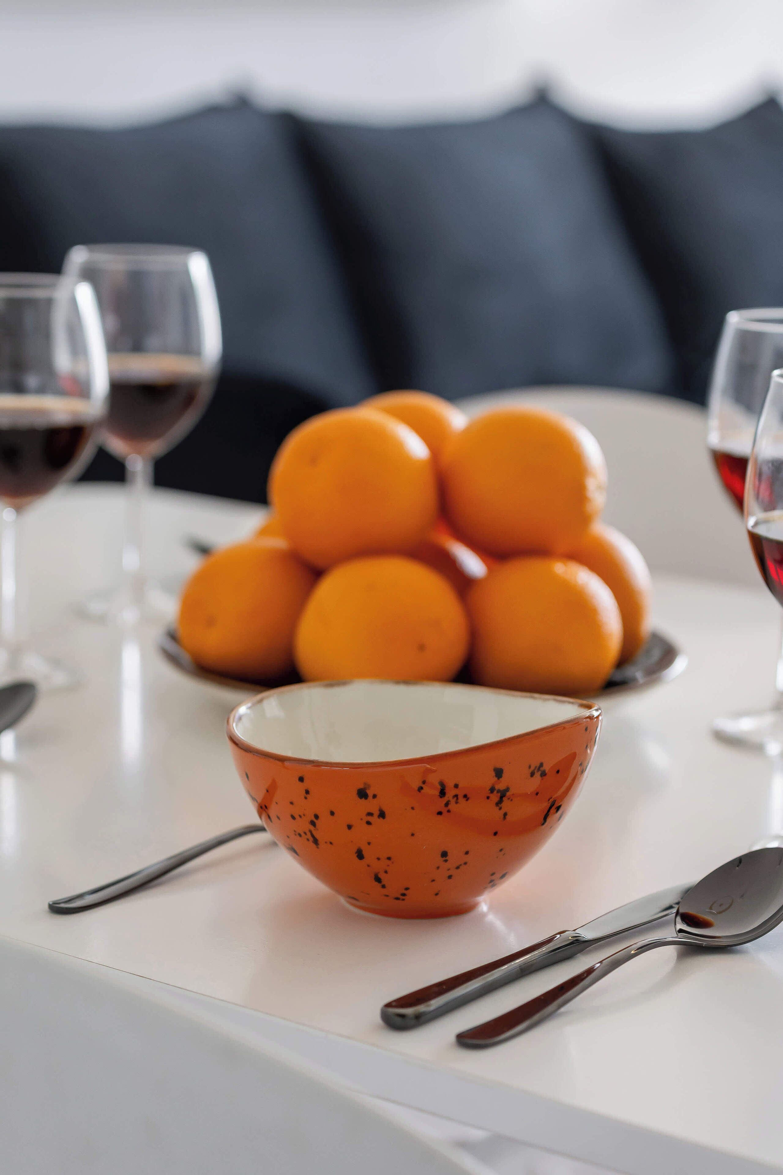 Une table avec un saladier rempli d’oranges, une assiette d’oranges et deux verres à vin.