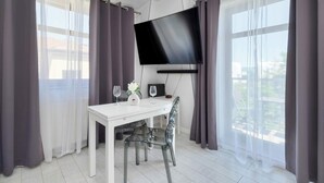 A modern room with a flat-screen TV mounted on the wall, a white table with two wine glasses and a vase, and a chair.