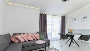 Una sala de estar moderna con un sofá gris, una mesita redonda y una zona de comedor con una mesa y sillas negras.