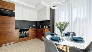 Une cuisine moderne avec des meubles en bois, un four encastré et un coin repas comprenant une table ronde et des chaises.