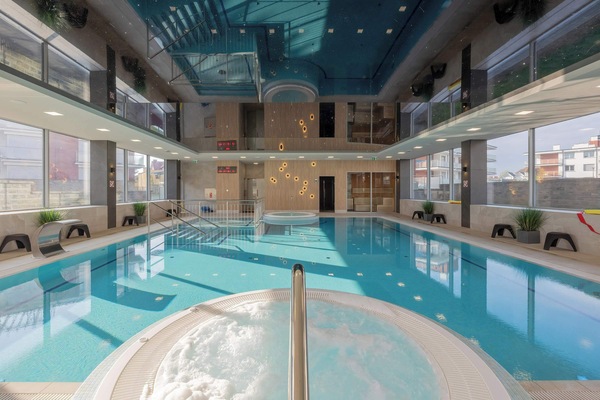 A warm indoor pool area featuring a large jacuzzi and multiple leisure zones.